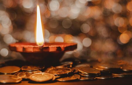 Matte effect. A terracotta lamp lit up with a straight and erect flame and round bokeh in the background, with coins aroundの写真素材
