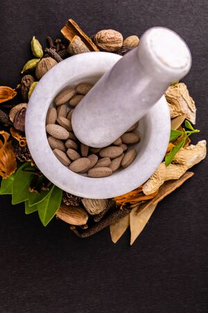 Top view of white mortar pestle crushing brown tablets with scattered whole spices and herbs on a black background, ayurveda conceptの写真素材