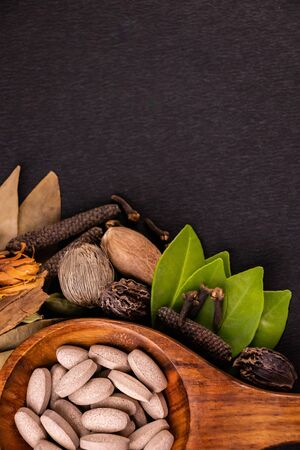 Traditional medicine concept, close-up of herbal pills in a wooden spoon shot from the top and different spices, green leaves on black background with copy spaceの写真素材