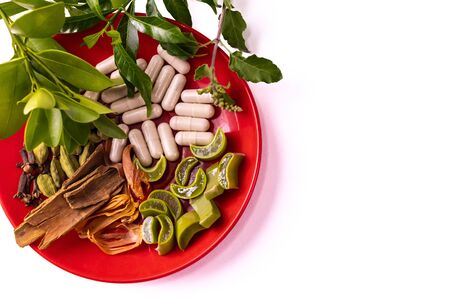 Creamy white herbal capsules, green ocimum leaves and sliced aloe vera in a dish on white backgroundの写真素材