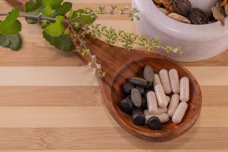 Top view of ayurvedic medicine in wooden spoon with assorted Indian Spices with green leaves on wooden background. Herbal medicines conceptの写真素材
