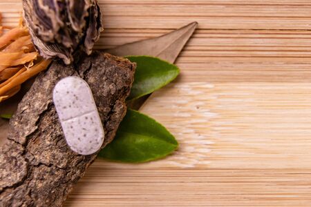 Herbal medicine concept. Top view of a single white ayurvedic tablet with green leaves, cinnamon stick, black and green cardamom with seeds on wooden backgroundの写真素材