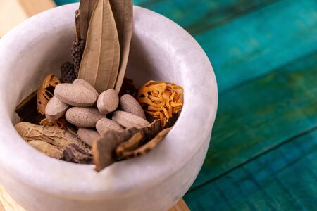 high angle macro shot of mortar with herbal tablets in dried herbs against bluish green background....