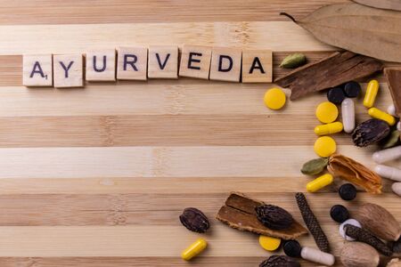 Ayurveda word written on wooden blocks with dry herbs and spices against wooden background. Unani...