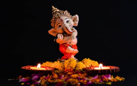 beautiful photography of ganpati statue with two glowing lamp and flowers on the black background. hinduism conceptの写真素材