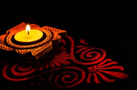 high angle view of awesome clay lamp and red rangoli art on black background with copy space. diwali...