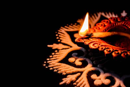 high angle view of awesome shining diya and white rangoli art on black background with copy space in...