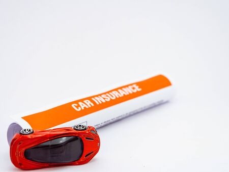 A rolled car toy and roll of insurance papers shot on white background from high angle pointの写真素材