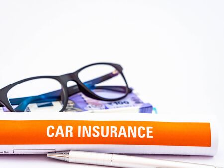 An eyeglass over money stacked along car insurance document and ball pen showing a wise decisionの写真素材