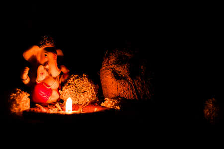 low light photography of ganesha statue with glowing diya on rose petals against dark blurry background. religious conceptのeditorial素材