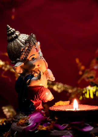 high angle photography of ganesha statue with earthen lamp on flower petals against red chunari in the background. religion and hinduism conceptのeditorial素材