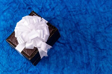 Small brown colored gift box with white ribbon bow and blue background. Wedding gifts concept