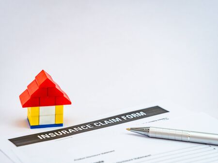 house toy with insurance claim form and a ball pen shot on white background with copy spaceの写真素材