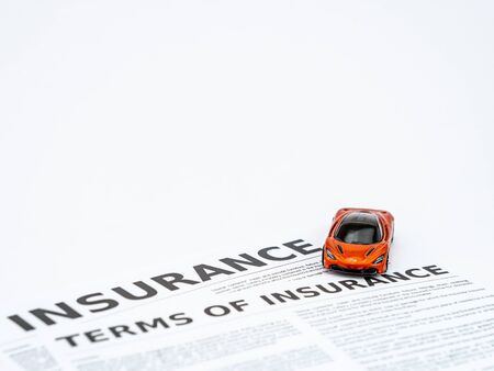 High angle view of a small toy car on insurance papers shot against white backgroundの写真素材