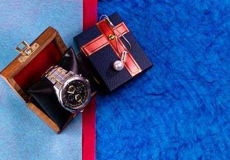 High angle close up shot of a blue gift box and wrist watch in wooden case on blue background, Couples gifts conceptの写真素材