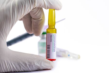 A human hand wearing gloves holding a generic ampoule labelled Corona Virus Vaccine