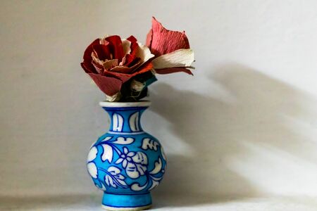 Front close up shot of a blue flower vase with red colored flowers made of craft paper and copy...