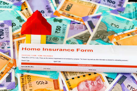 Close up shot of a Home Insurance Document rolled on scattered notes with a small house