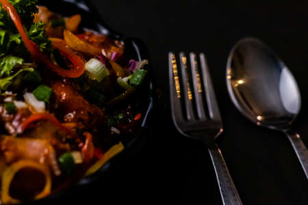 Photography of delicious Chilli chicken with spoon and fork on black surfaceの写真素材