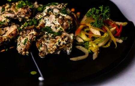 High angle close up of tasty Chicken Malai Tikka garnished with colourful veggies.の写真素材