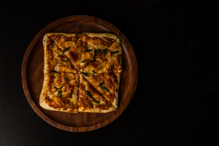 Top angle shot of tasty pizza kept on wooden plate and dark in background.の写真素材