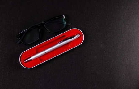 Top shot of an eyeglass with a silver ball pen in its case over black background for graduation and higher study conceptの写真素材