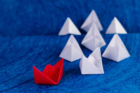 High angle shot of one red and few white paper boats on blue textured paper as sea