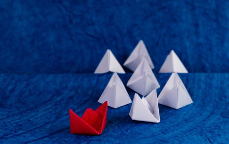 High angle shot of one red paper boat with white boats on blue textured paper as oceanの写真素材