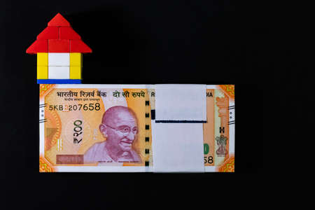 A small toy house on bundle of two hundred rupee notes over black background in Home Loan concept