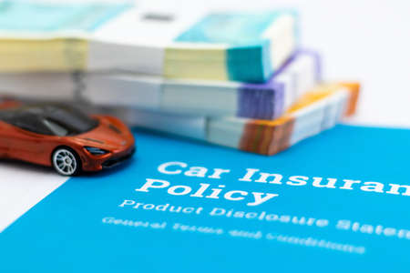 Closeup shot of a small toy and car insurance papers with bundles of money defocused in the backgroundの写真素材