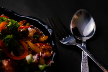 High angle close up of delicious Chilli chicken with fork and spoon on black surface