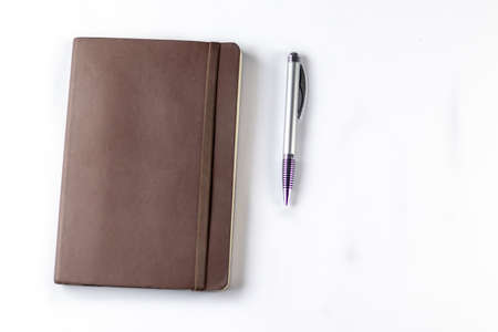Top shot of a spring operated ball pen and brown colored diary with elastic band shot over white background in accounting conceptの写真素材