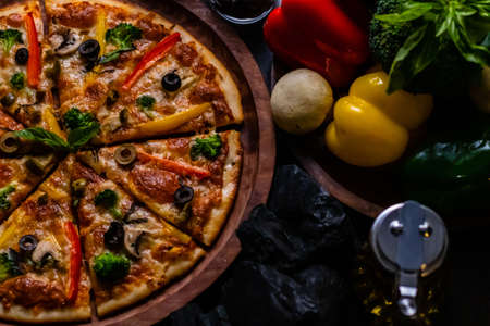 Close up shot of delicious pizza along with colorful vegetables, coal and olive oil jarの写真素材