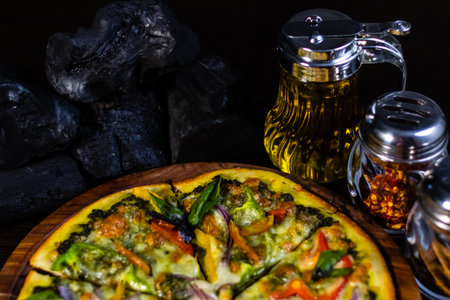 High angle shot of Hawaiian Pizza full loaded with fresh vegetables and charcoal in a background.の写真素材
