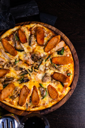 Portrait shot of yummy Chicken Pepperoni Pizza in wooden pan and kept in dark surface.の写真素材