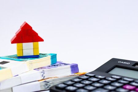 Low angle close up of a defocused calculator with one home and money bundles shot against white backgroundの写真素材
