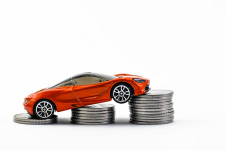 Simplistic shot of an orange toy car placed on the column of coins in automobile industry concept.の写真素材