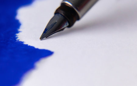 A fountain pen nib in close up with blue ink spread on blank white paper sheet