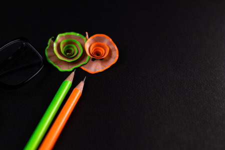 High angle shot of two pencils with their shavings and a spectacle on black background.の写真素材