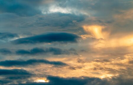 Abstract background, scenery of dramatic sky in evening, with storm clouds, blue, grey, orange, golden light in twilight, and sunlight breaking through clouds, looks like watercolor painting.の写真素材