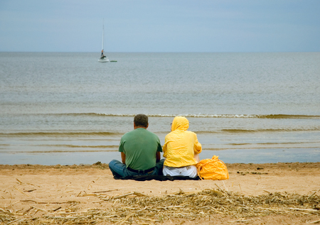 Lonely couple sitting on the beach and looks into the distanceの写真素材