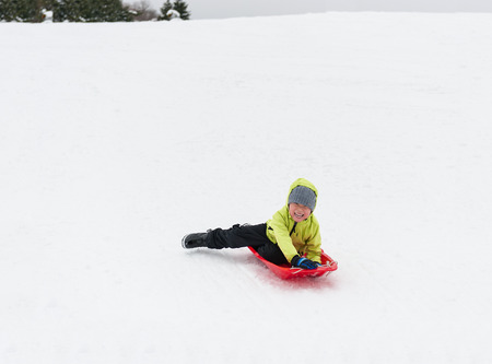 Cute young boy smiling while he is sledgingの写真素材
