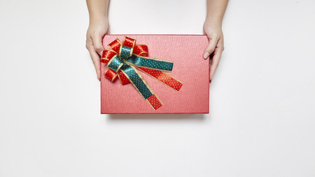 female hand in sweater holding a red present box for Christmas, New Year, Valentine'a day on white background, top view with copy spaceの写真素材