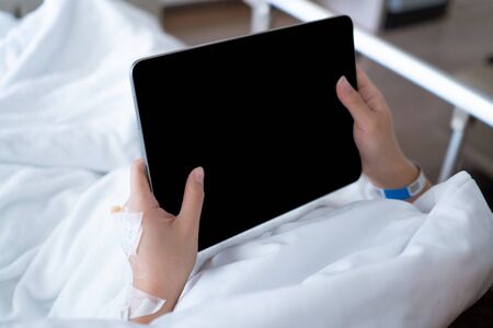 close up patient hand using digital tablet while lying on bed in hospital, technology and medical conceptの写真素材