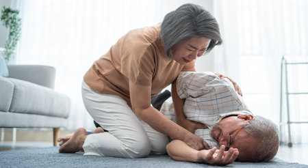 Asian senior wife helping husband fainting and falling on the ground in the living room. Elderly...
