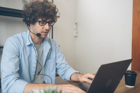 Male agent or telemarketing in eyeglasses with headphone talking to customer working at home. Man meeting video call work remotely on weekend. Teacher teaching or consulting online.の写真素材