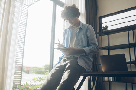 Businessman or creative freelancer writing on digital tablet. Man study online and note on the device at home. People connecting with technology working remotelyの写真素材
