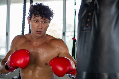 Caucasian muscular strong man in boxing gloves training exercise in gym fitness. Boxer workout punching bag fist. fighting sportの写真素材