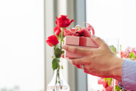 Man hand holding present box giving to girlfriend for Valentine's day, birthday or anniversary. Surprising gift on engagement or special eventの写真素材