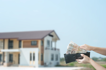 Property buyer holding Thai banknotes and buying beautiful house on blurred background.の写真素材